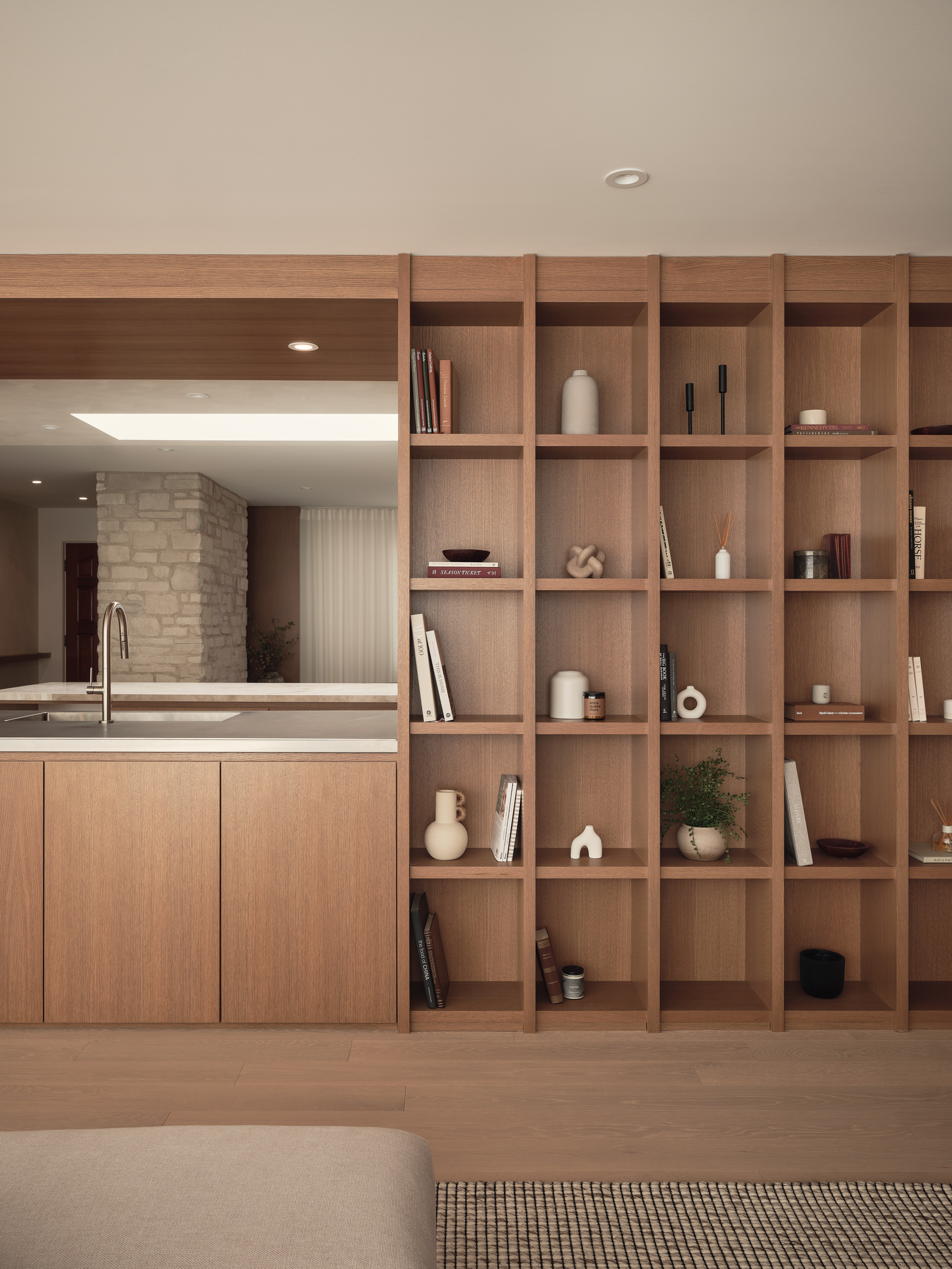 An open wooden bookshelf in the kitchen, featuring books, ceramic vases, and decorative items