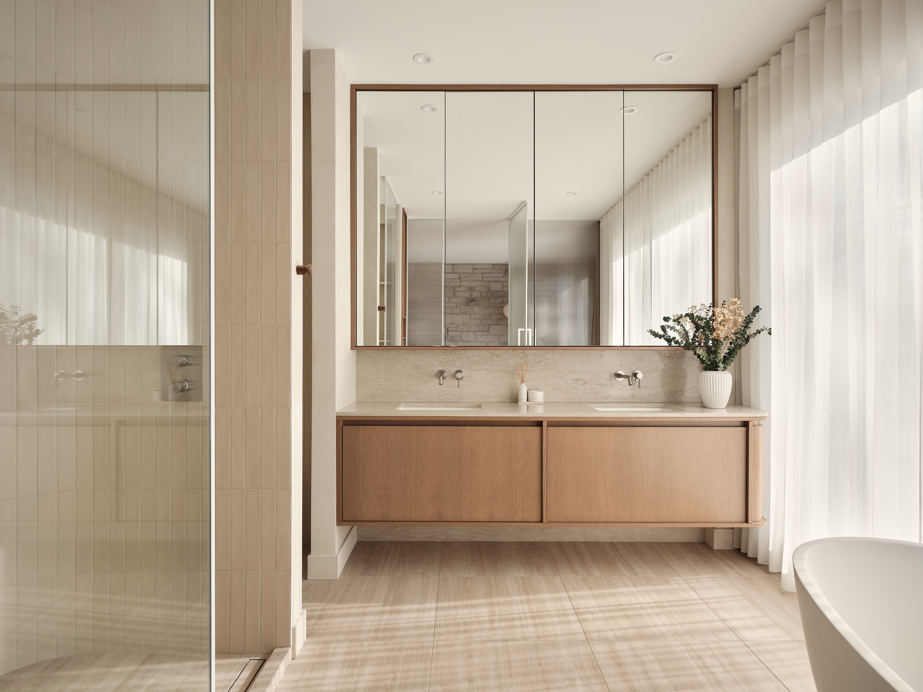 Bathroom with a double sink, full-width mirror, and a freestanding bathtub in the background