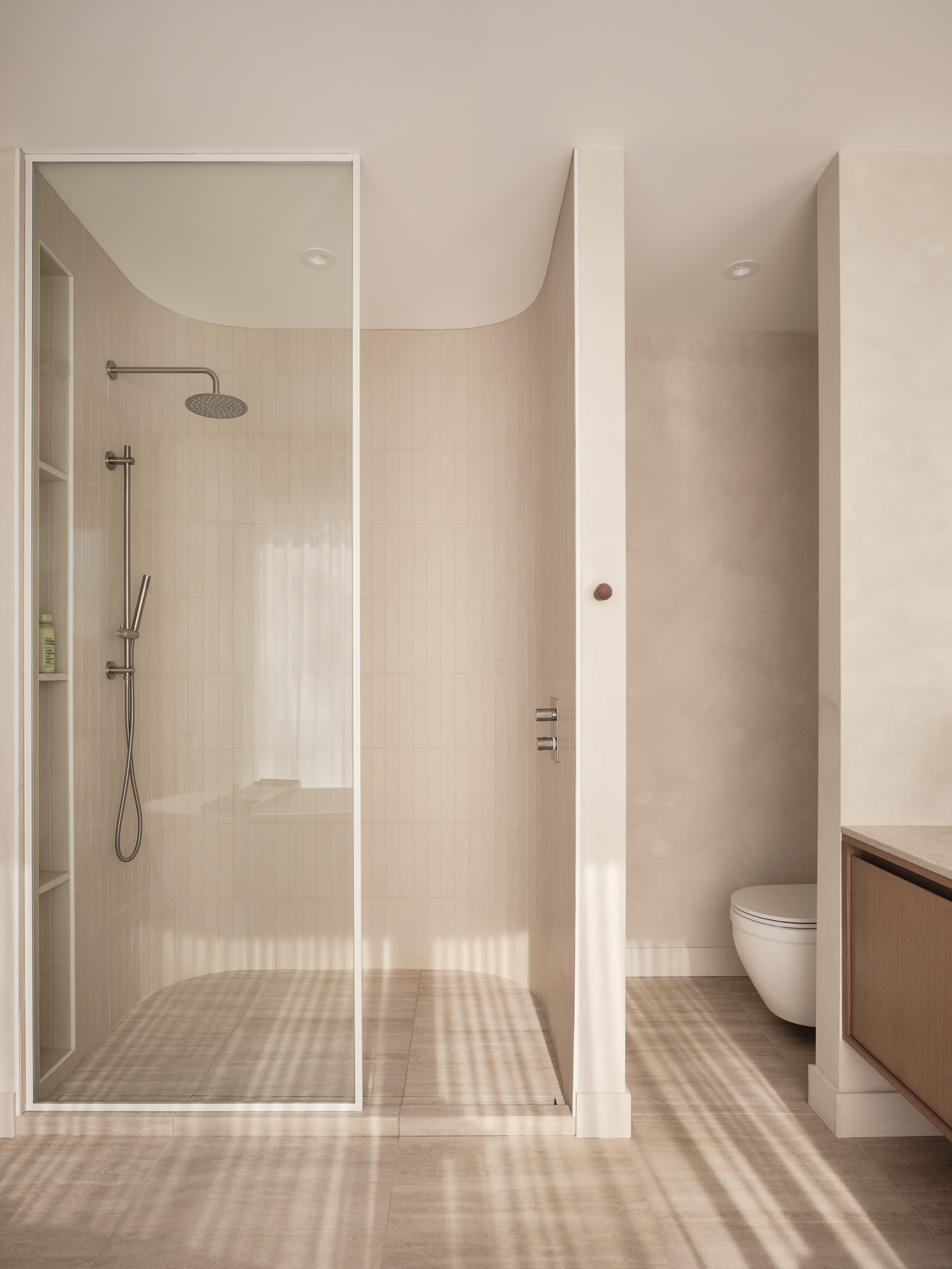 Glass shower with beige ceramic tiles and a toilet in the background