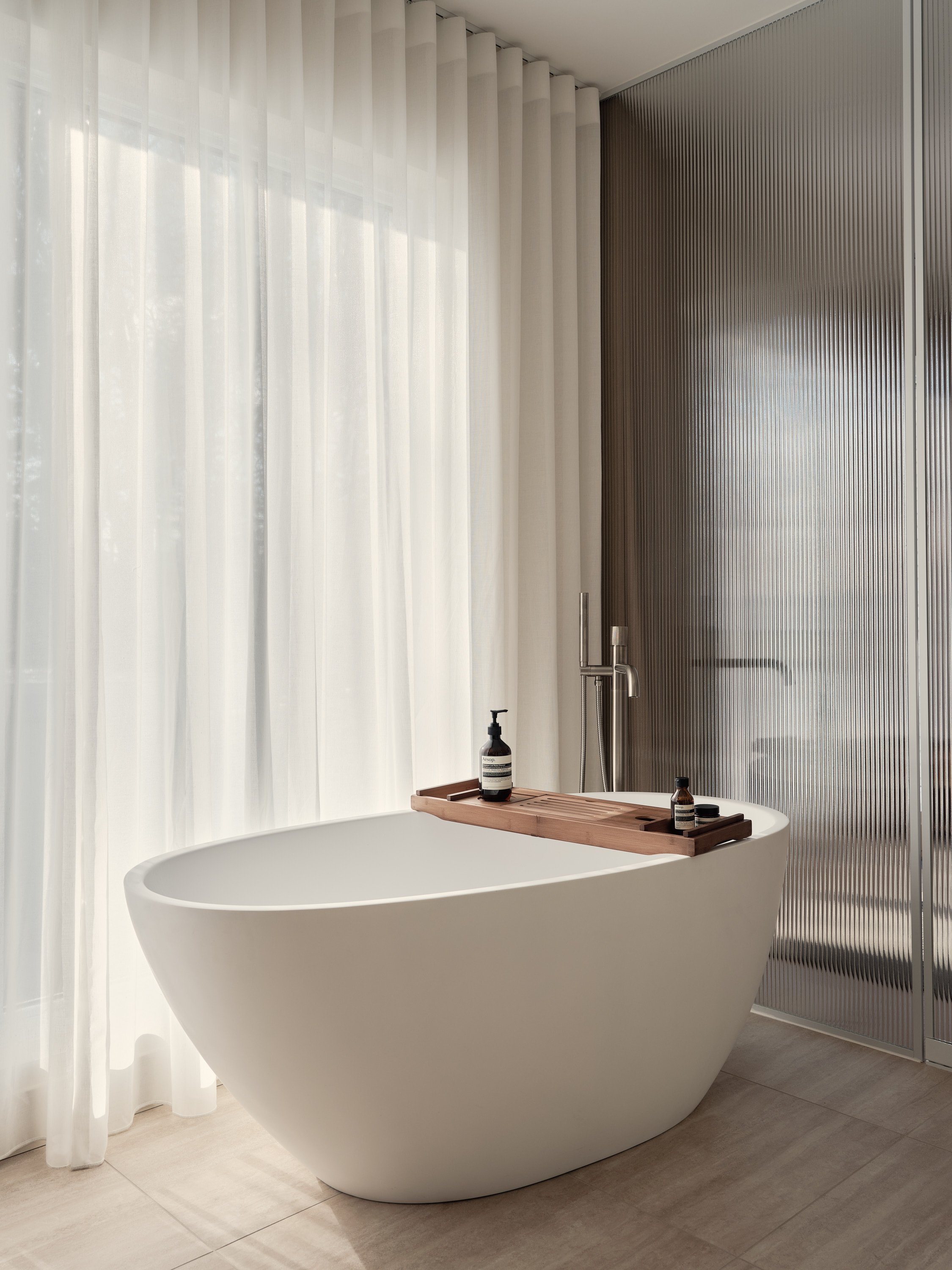A white freestanding bathtub in front of a window draped with sheer curtains