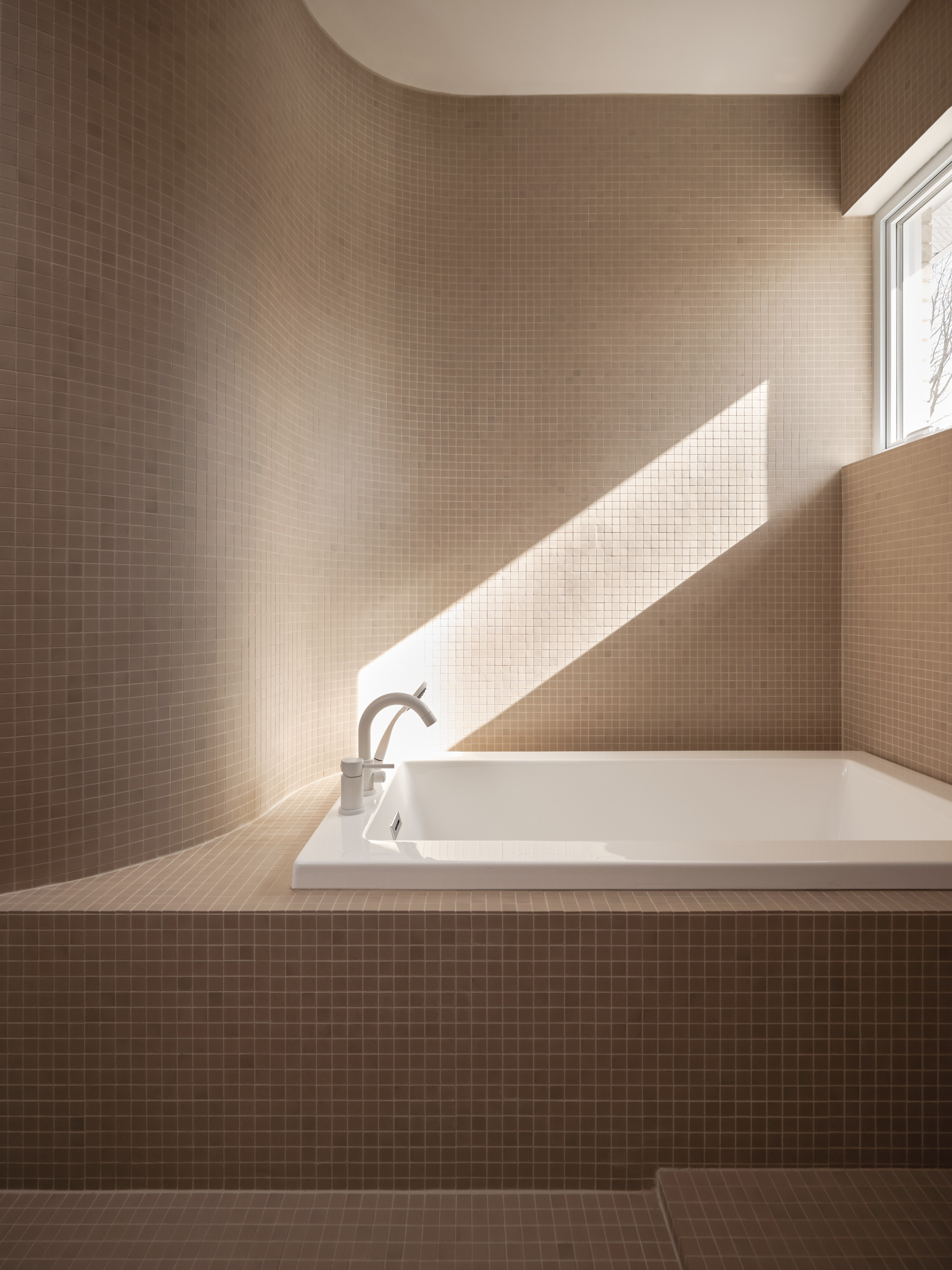 Secondary bathroom with a built-in mosaic bathtub and natural light