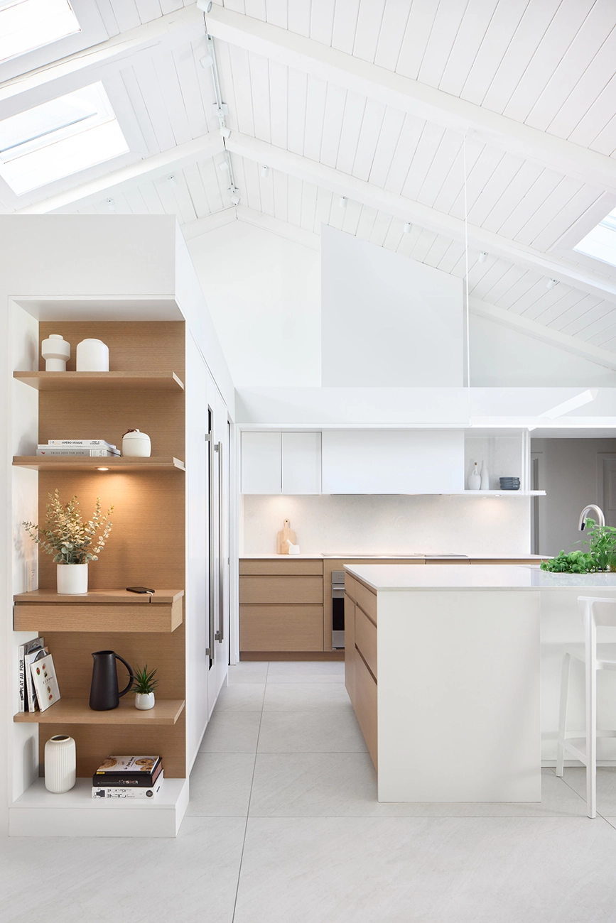 Built-in oak shelving with a cathedral ceiling featuring a skylight and a kitchen in the background