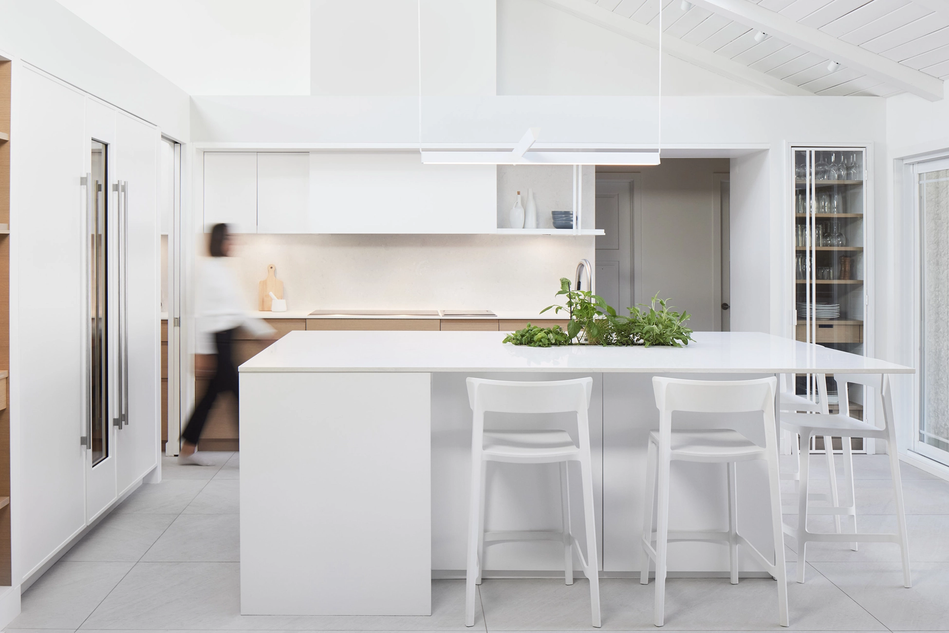 A sleek white kitchen with a glass-fronted oak wine cabinet and a central island