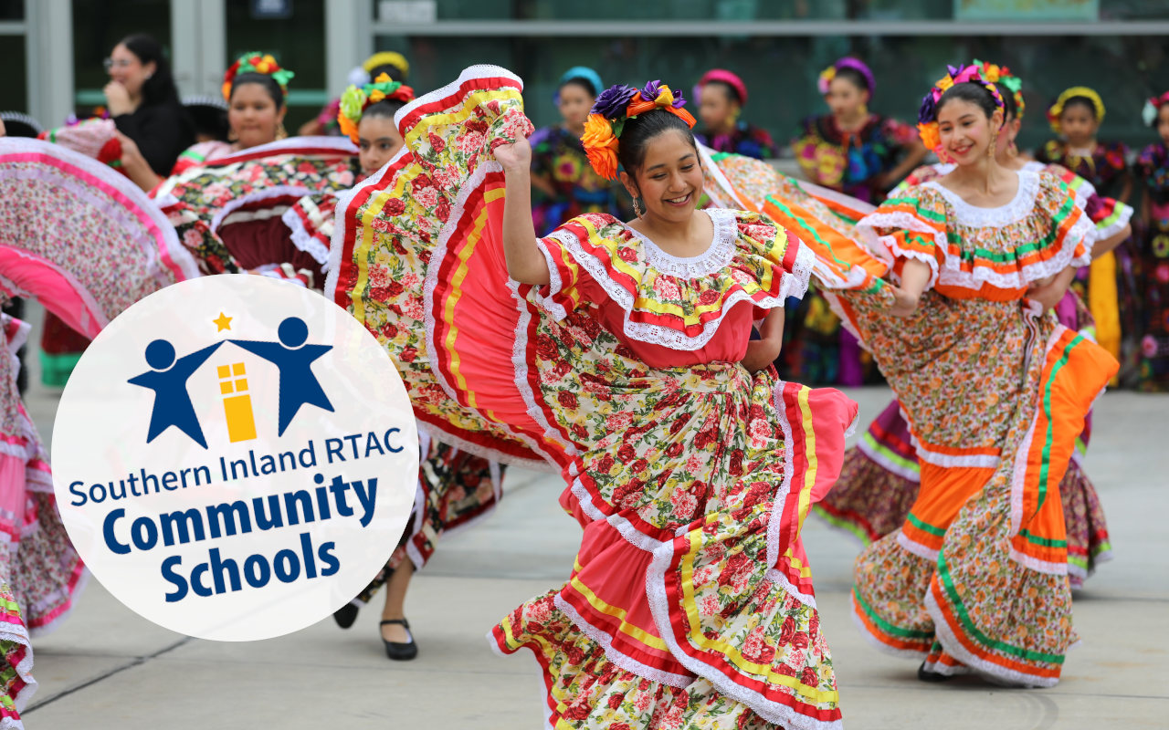 Brightly colorful photograph of 5 women dancing in traditional Mexican folkloric dresses, apparently in a street performance on the civic plaza.