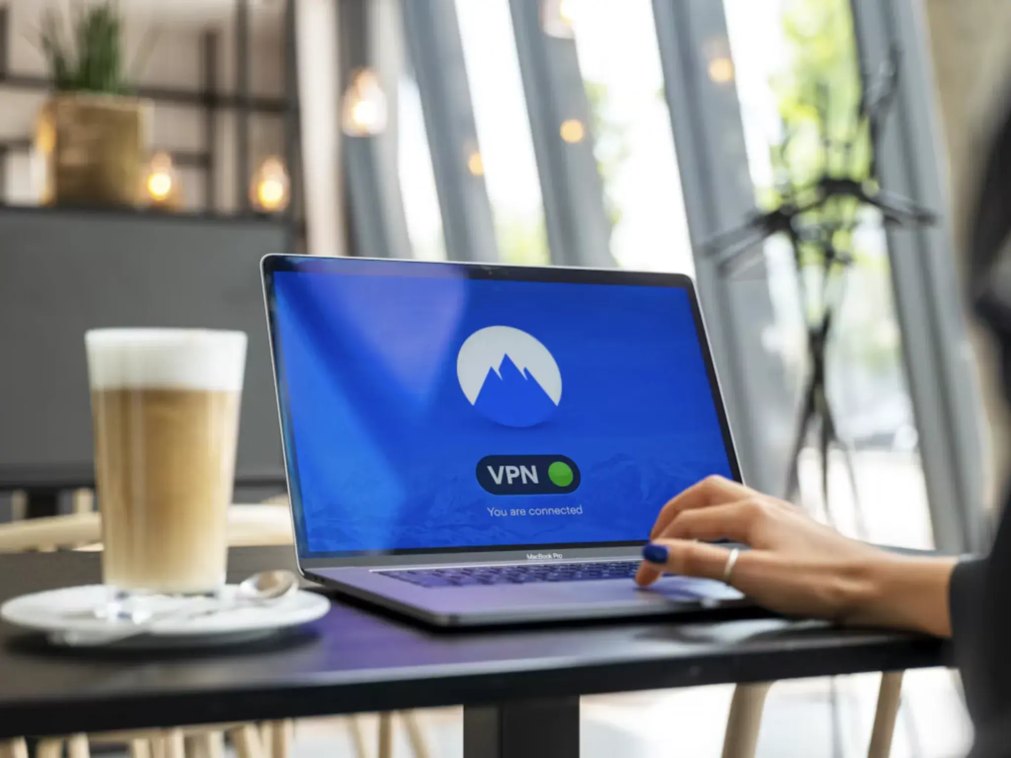 Remote worker connecting to a VPN on a MacBook Pro in a coffee shop, showing a secure connection confirmation.
