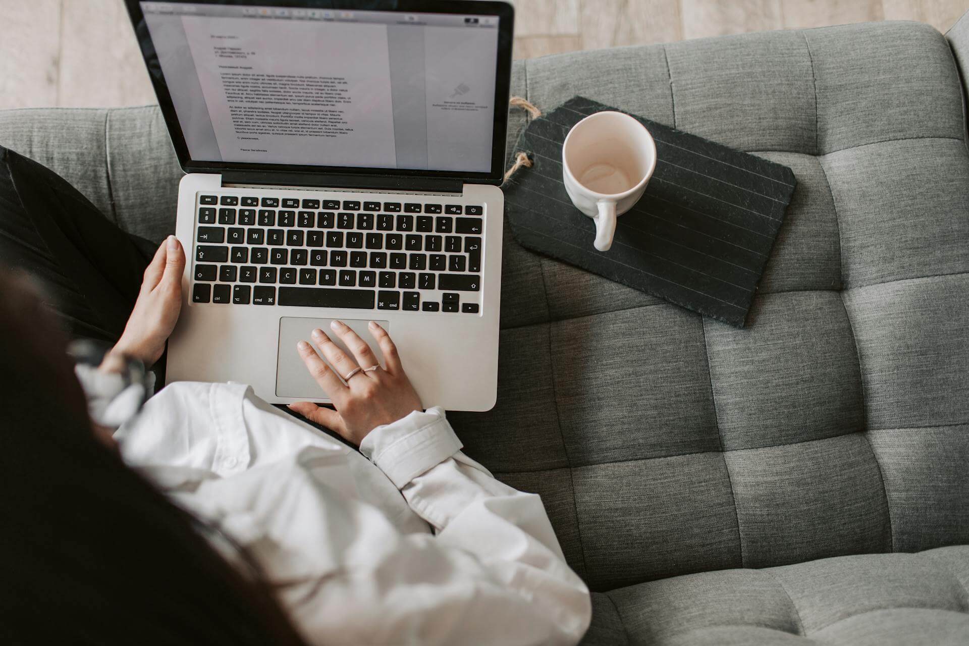 Photo of a person typing on a laptop with a cup of coffee nearby