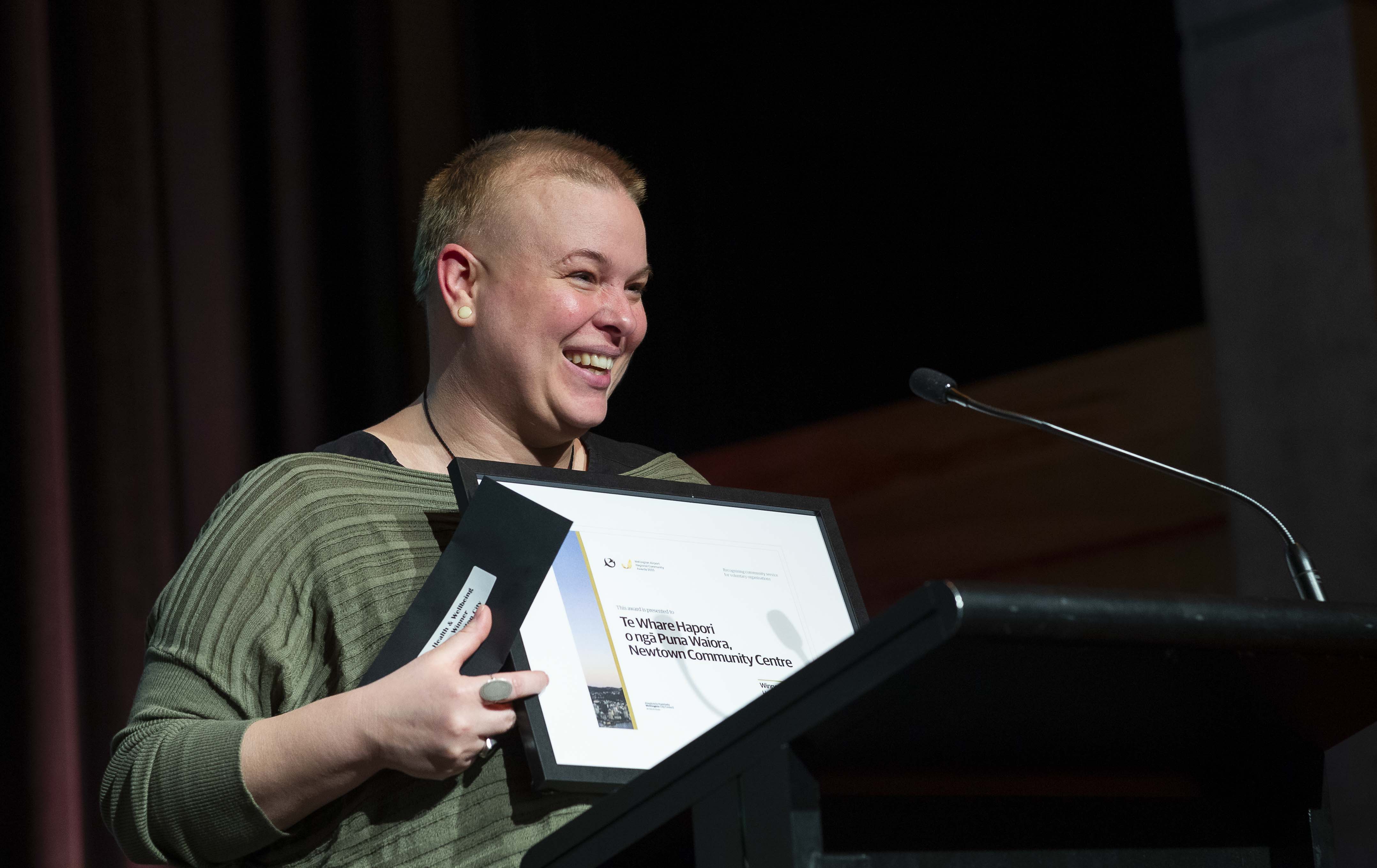 Anna is smiling an holding an award plaque at a podium.