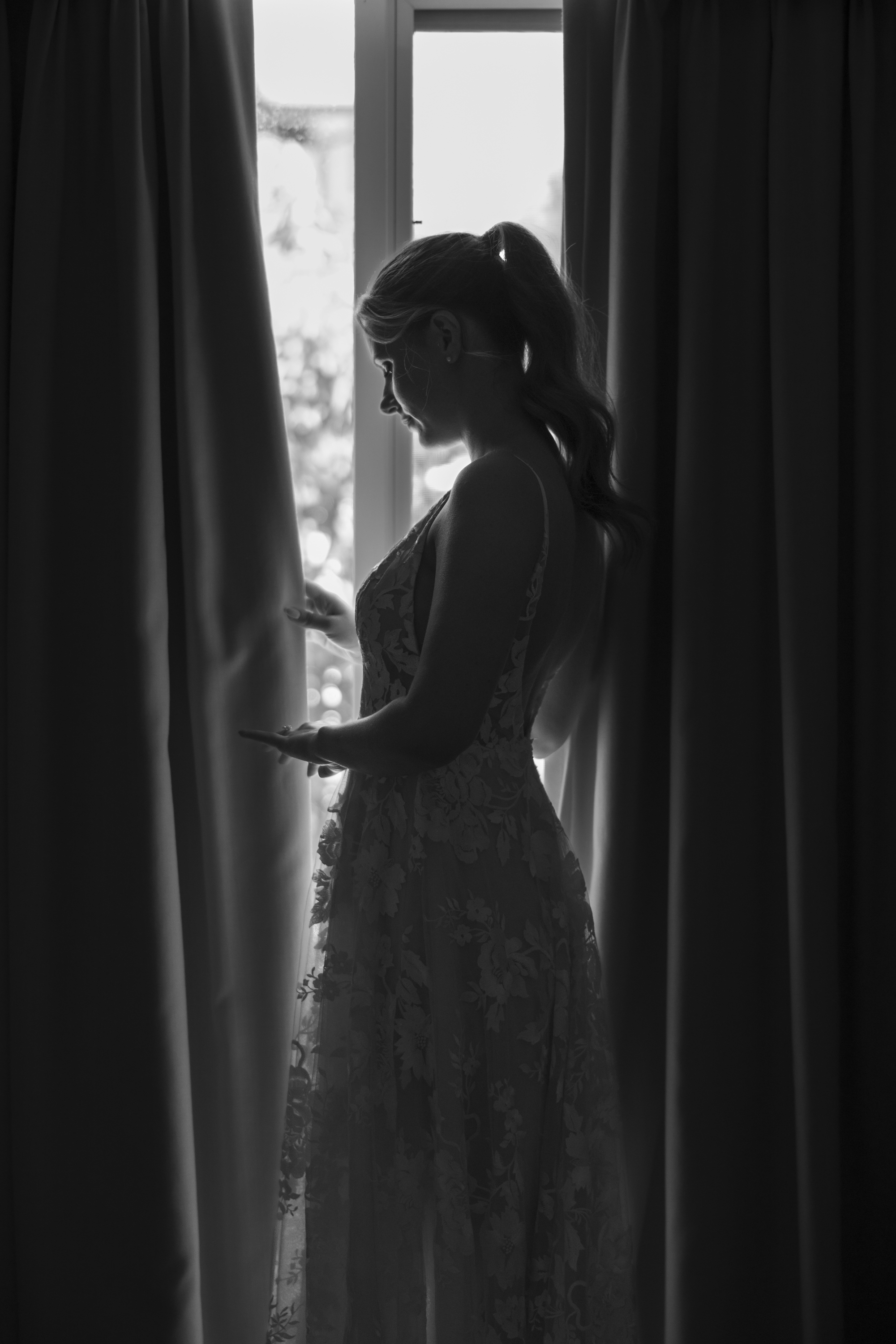 A woman in a lace dress silhouetted against a curtained window