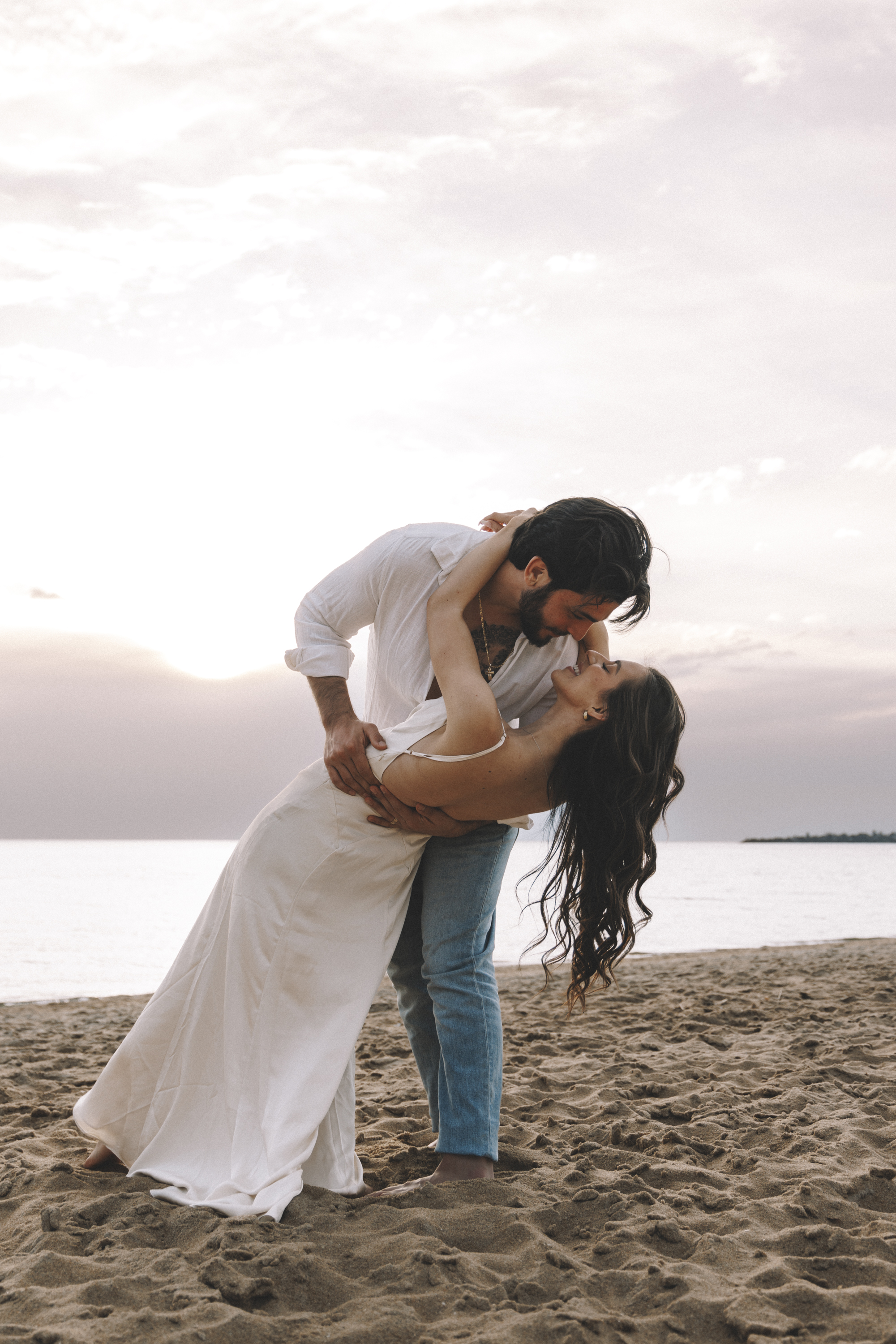 A man dipping his partner into a kiss on the sand at sunset