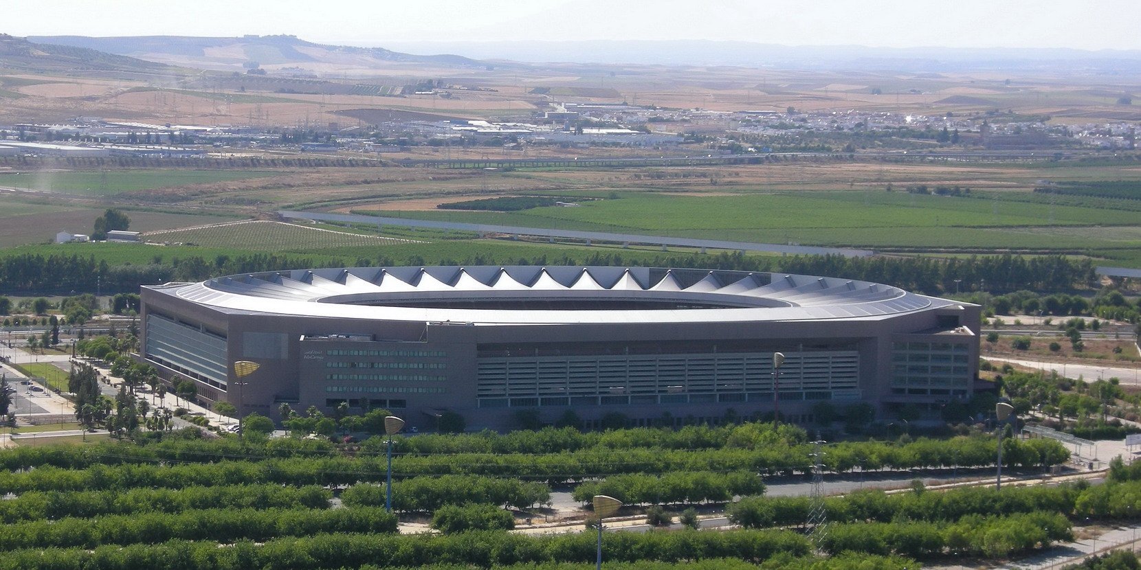 Vue aérienne du stade de La Cartuja à Séville, avec sa couverture blanche en dents de scie et la plaine du Guadalquivir en arrière-plan