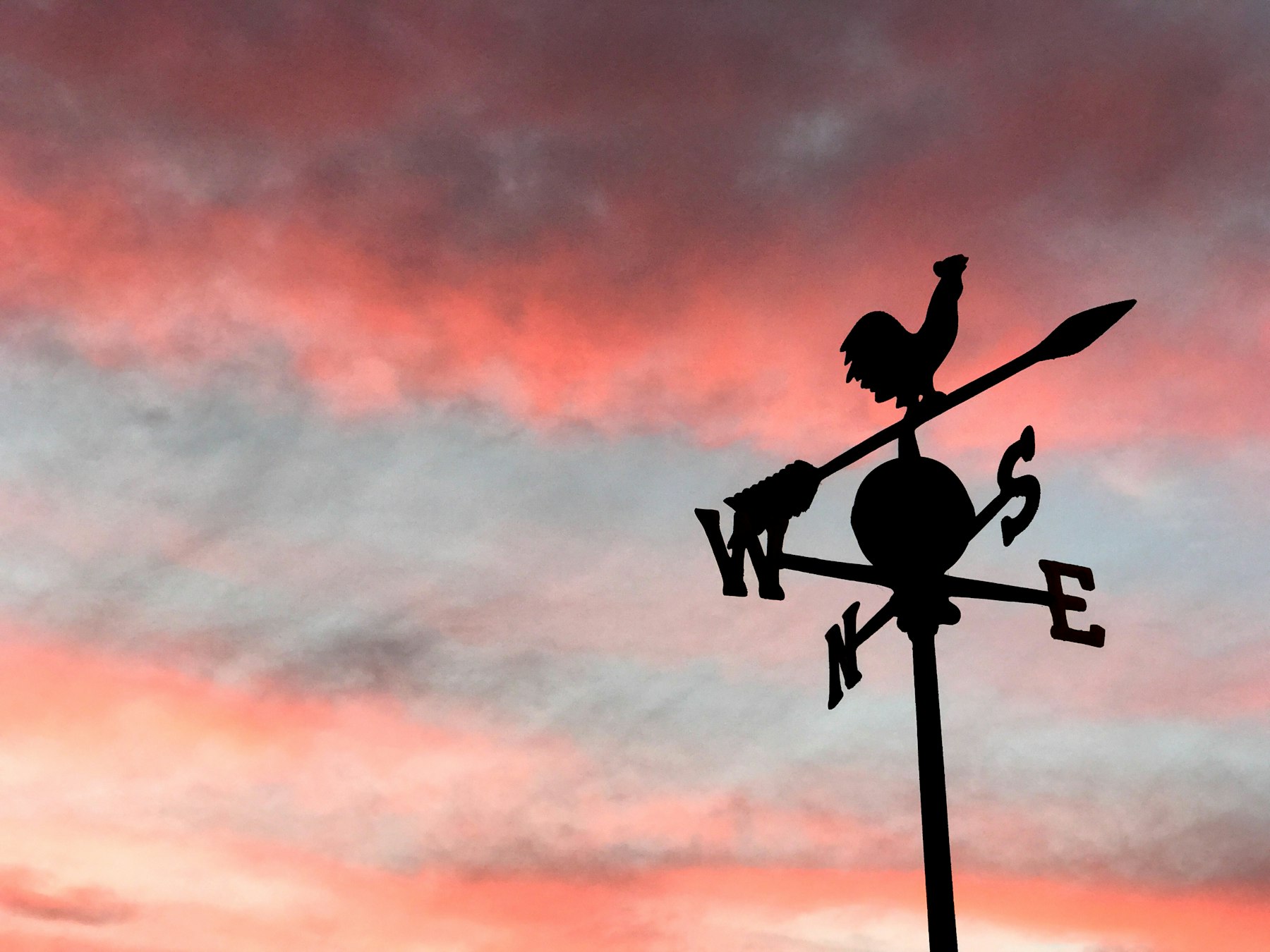 A rooster weather vane silhouetted against a pink sunset sky