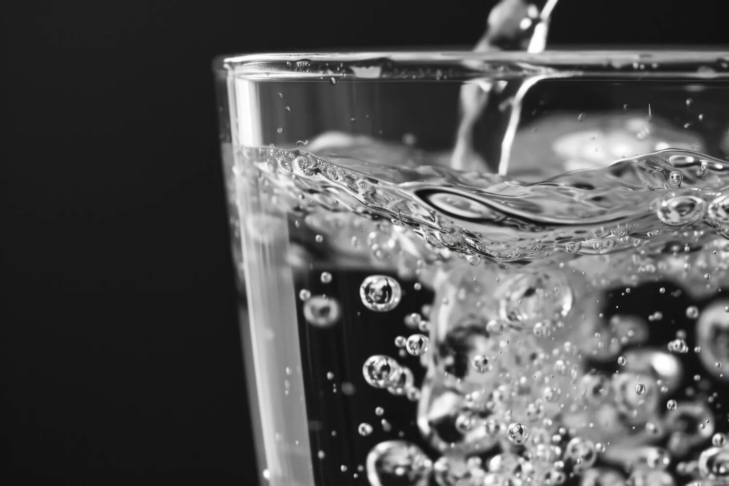 Close-up of sparkling water pouring into a glass with bubbles against a dark background.