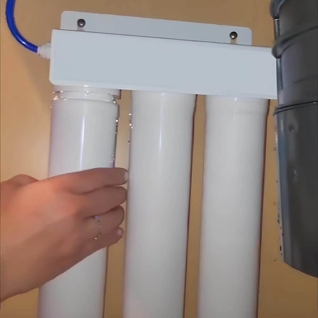 Hand adjusting a home water filtration system with three white filter cartridges installed under a sink.