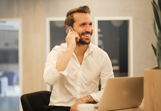 man speaking on phone while sitting in front of his laptop