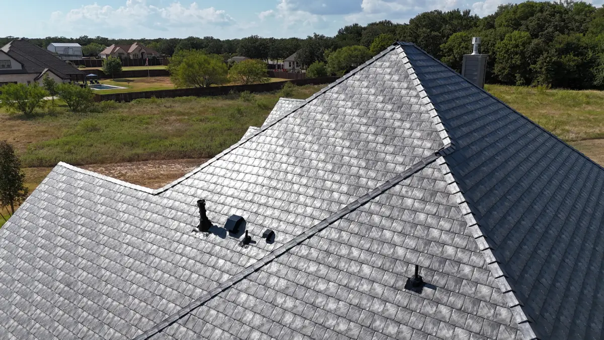 Aerial view of a large house roof with Euroshield installed on it, surrounded by green trees and neighboring houses.