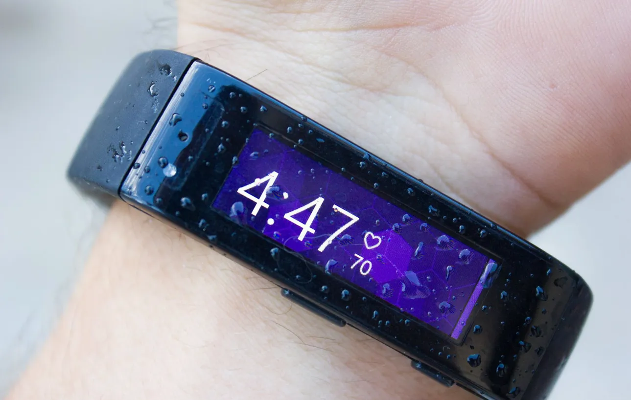A person's wrist wearing a black Microsoft Band displaying the time 4:47 and a heart rate of 70. Water droplets are visible on the watch and skin.