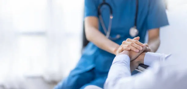 Healthcare professional in blue scrubs holding a patient's hand in a comforting gesture.