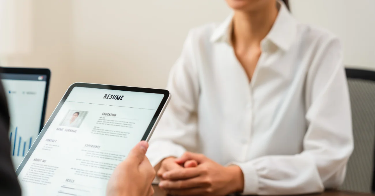 Person reviewing a resume on a tablet during a job interview with a candidate in a white shirt.