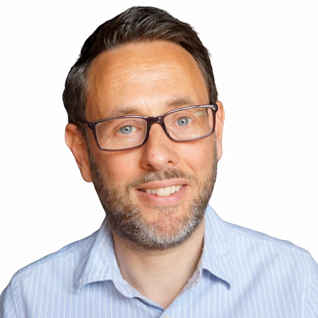 Smiling man with glasses, short dark hair, and a beard wearing a light blue striped shirt.