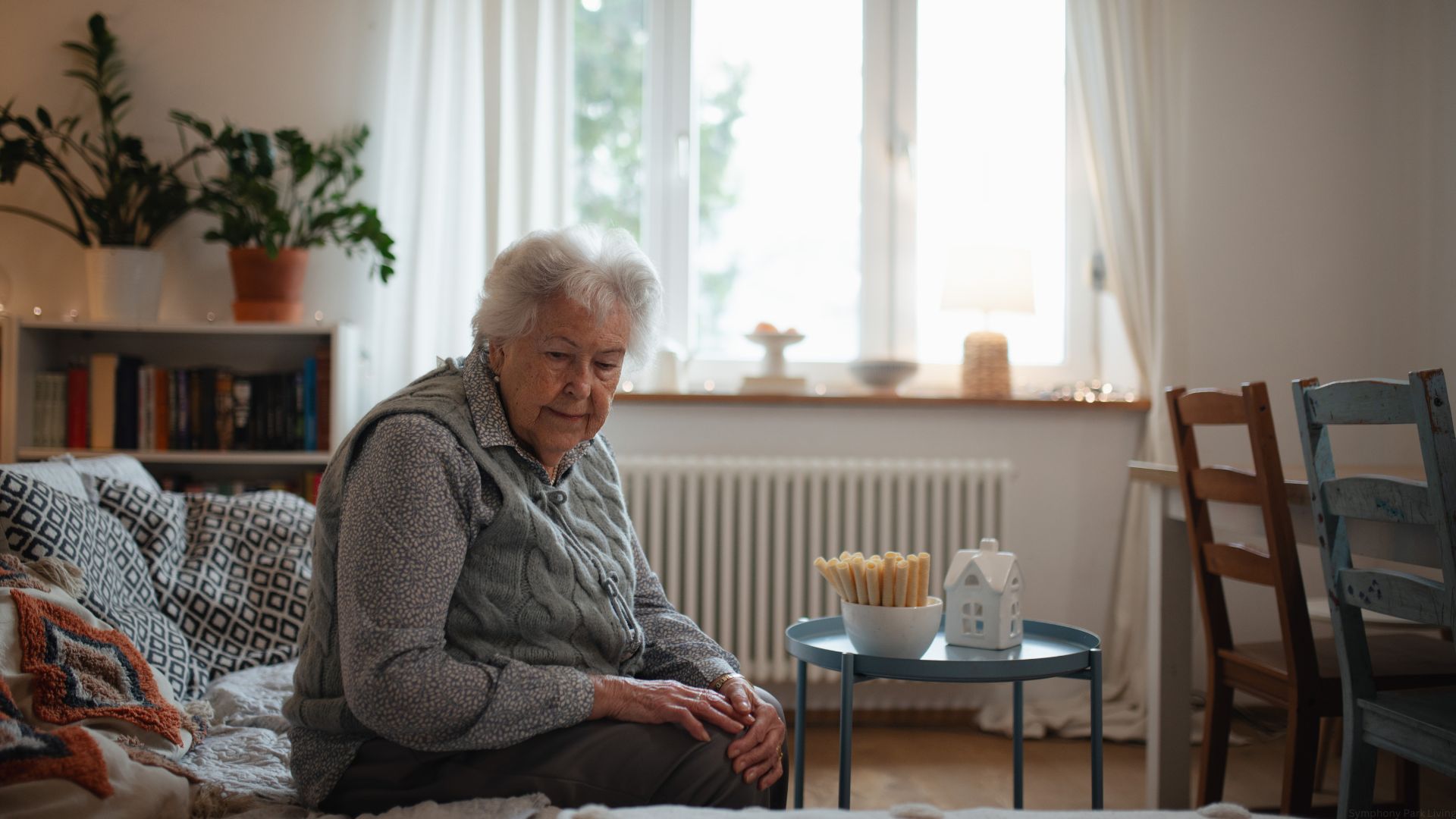 A senior who is aging at home sits alone on her sofa at home.