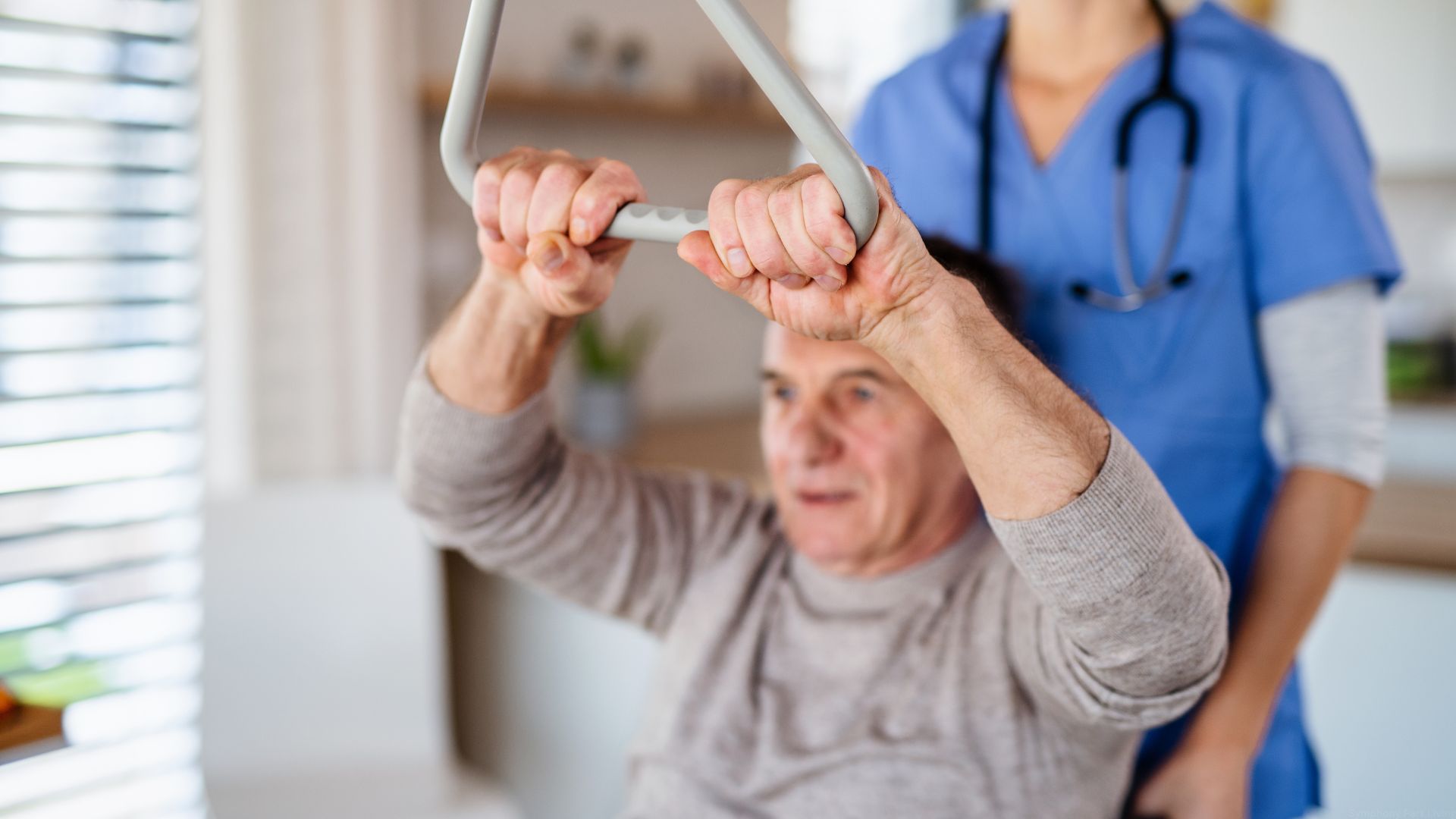 A senior man reaches for a handle while a physical therapist helps him.