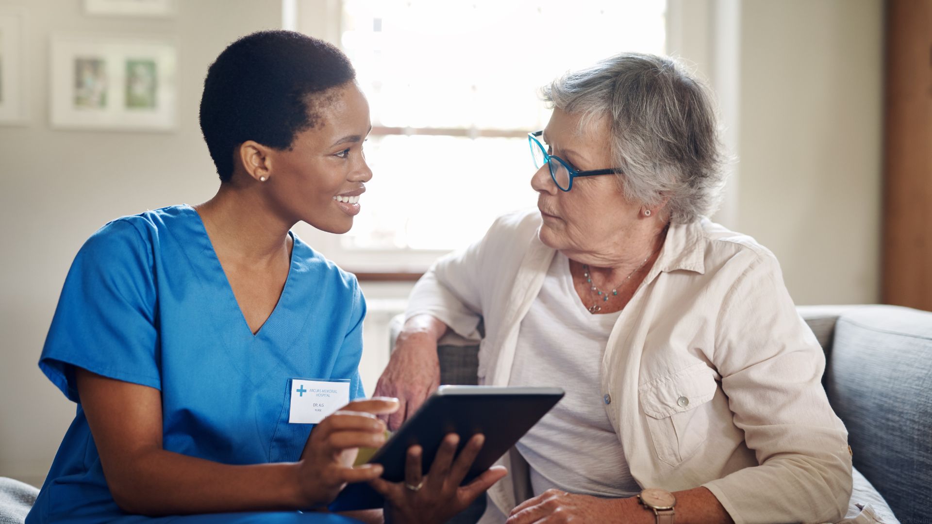 A geriatric care manager in blue scrubs meets with a senior patient.