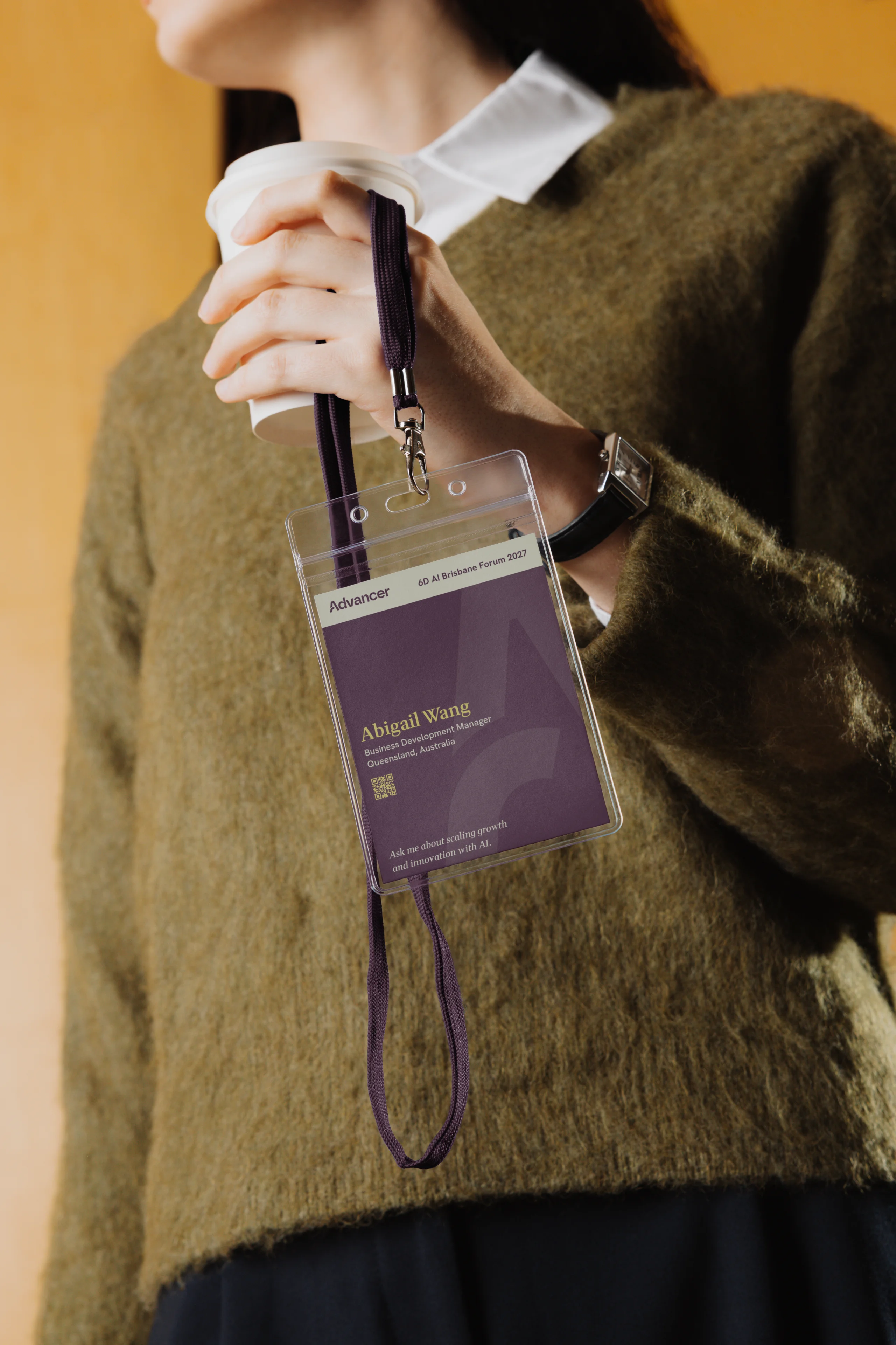 Person holding a coffee cup and a lanyard with a purple conference badge for Abigail Wang, Business Development Manager.