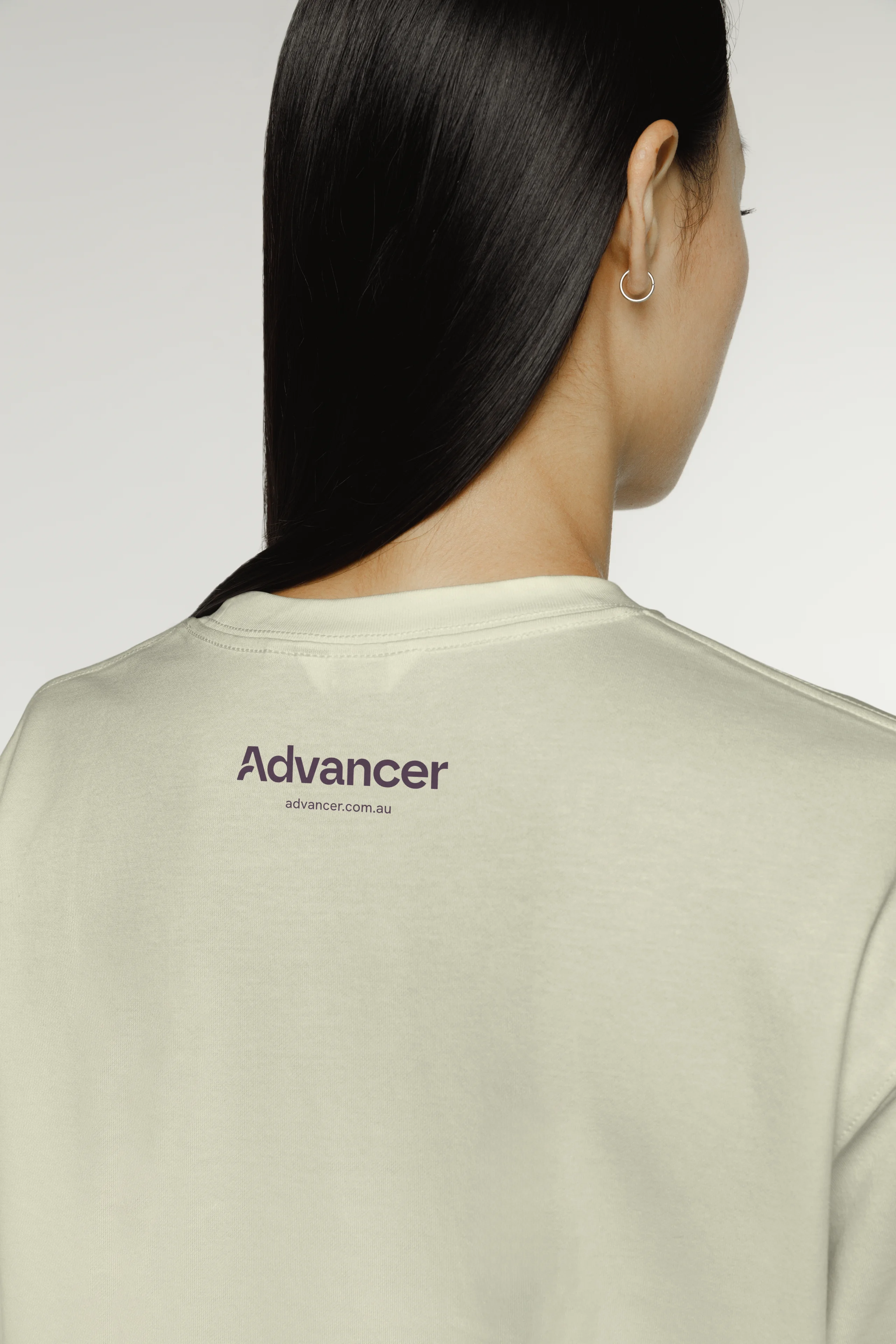 Back view of a person wearing a cream shirt with the Advancer logo and website near the collar.