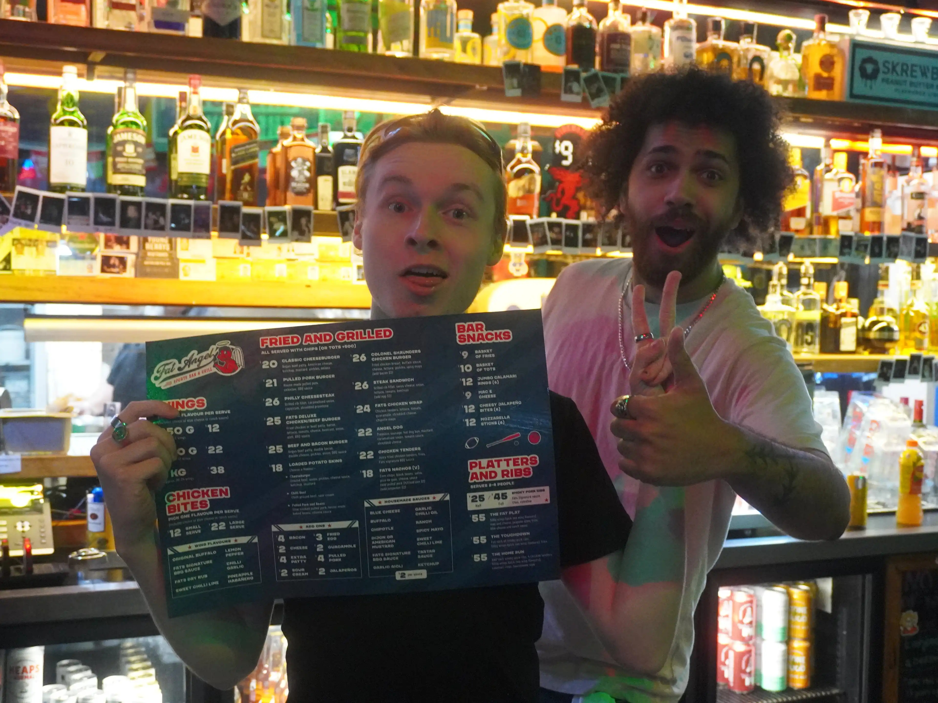 A photo of the menu being held by two of the bartenders of Fat Angel Sports Bar and Grill.