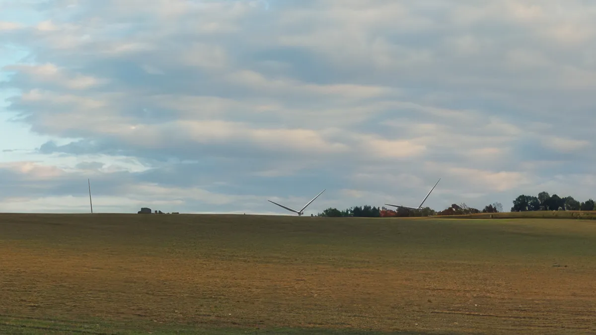 Pole a dvě větrné turbíny ležící na zemi v rozsáhlé poli pod oblohou s mraky.