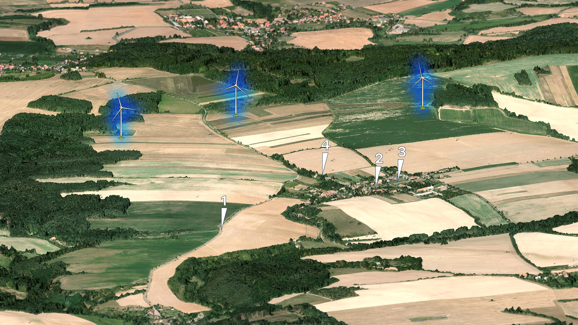 Letecký pohled na krajinu se zemědělskými poli, vesnici a třemi větrnými elektrárnami.