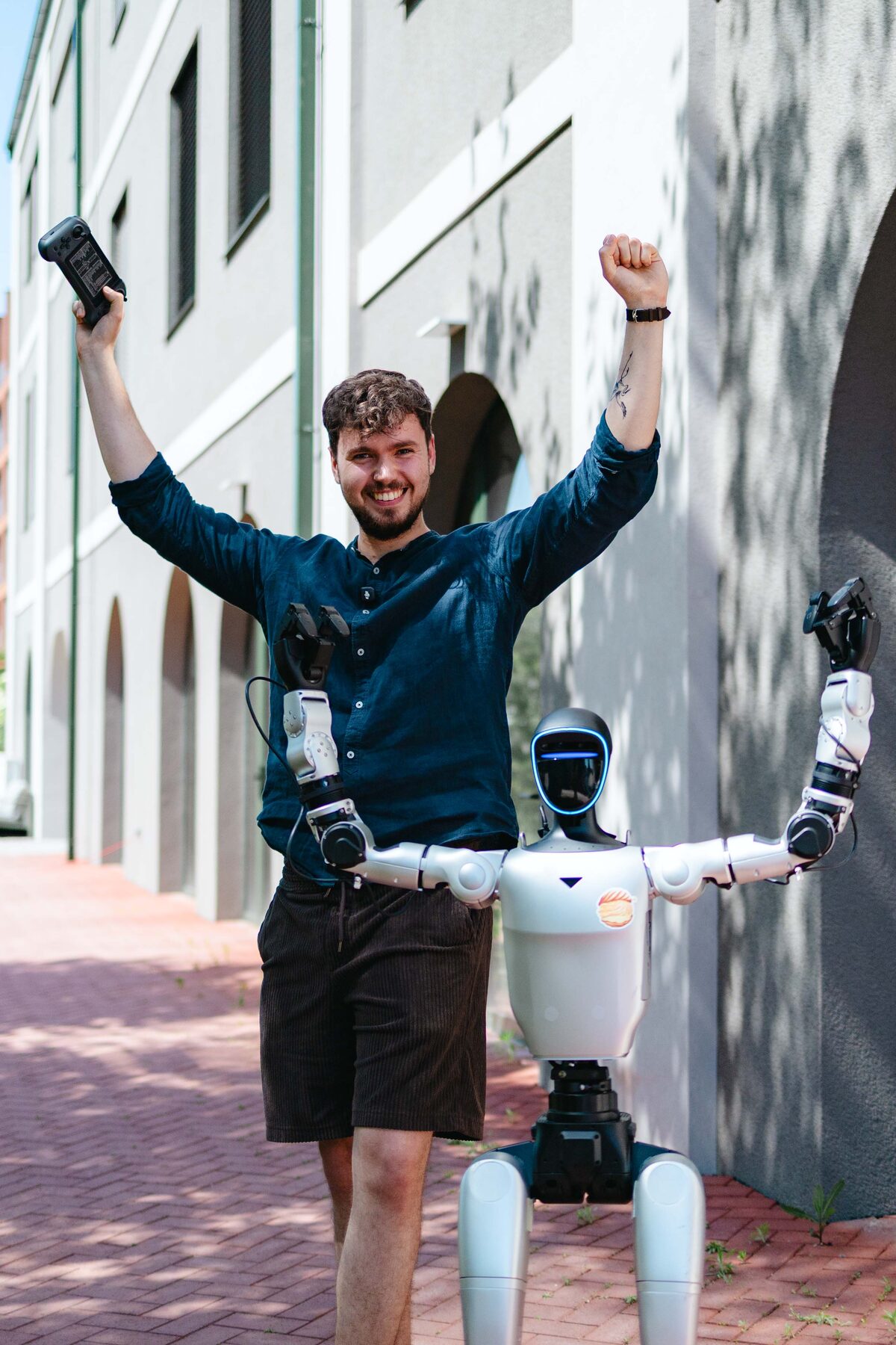 Kolega z NOHO se raduje se zdviženýma rukama vedle humanoidního robota