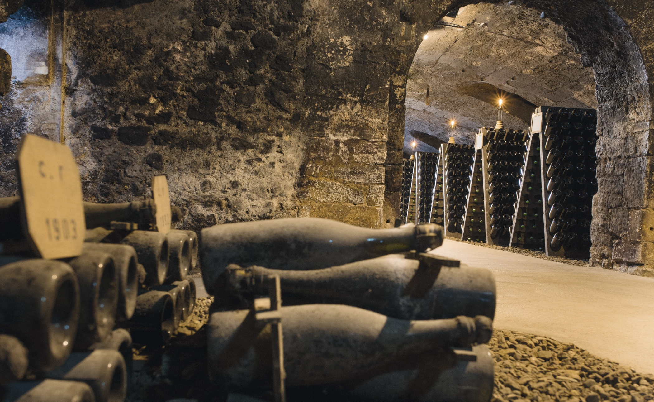 Bouteilles de vin poussiéreuses empilées dans une cave en pierre avec un éclairage tamisé.