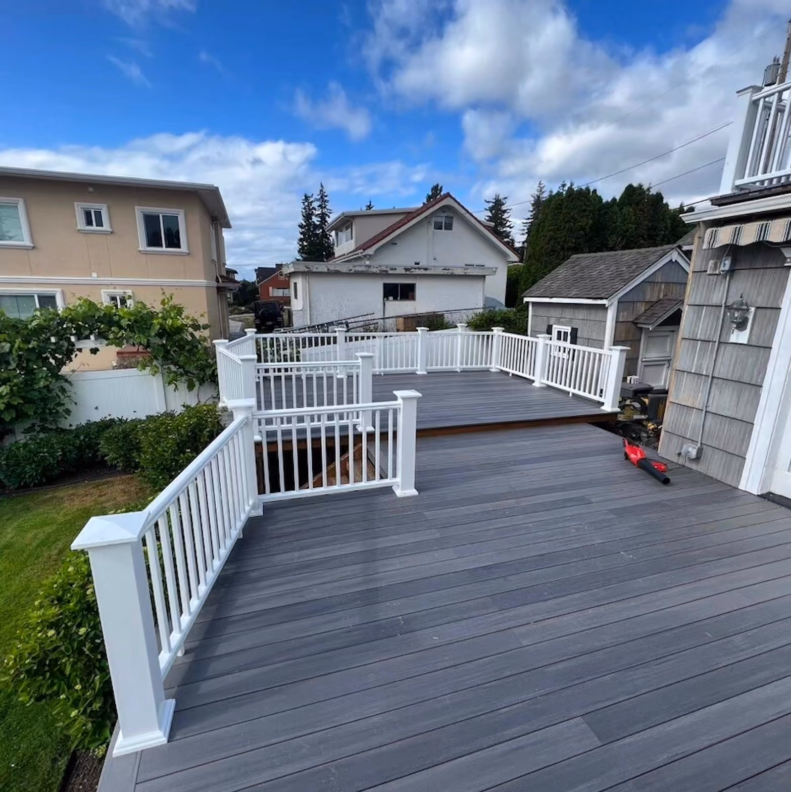 Spacious gray outdoor deck with white railings and a red leaf blower on the floor near the house.