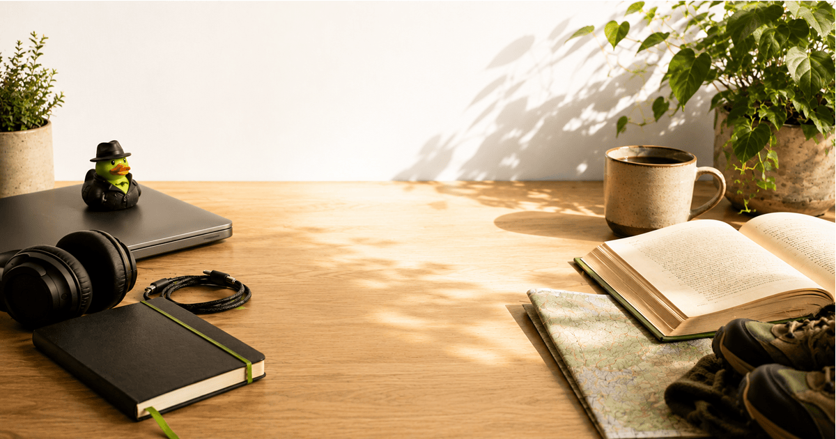 A warm, sunlit desk is arranged with a closed laptop, notebook, headphones, coffee mug, open book, hiking map, plants, and a small Test Double-themed rubber duck. A large open space in the center of the desk symbolizes the breathing room created when technology helps people reclaim time for thinking, rest, and life beyond work.