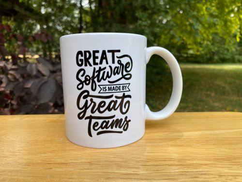 Mug reading Great Software is made by Great Teams sitting on a table in a lush backyard