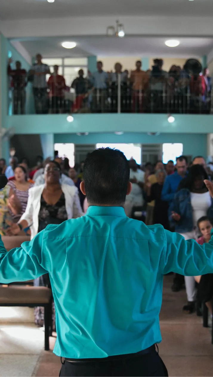 A man leads worship in front of congregation with arms raised