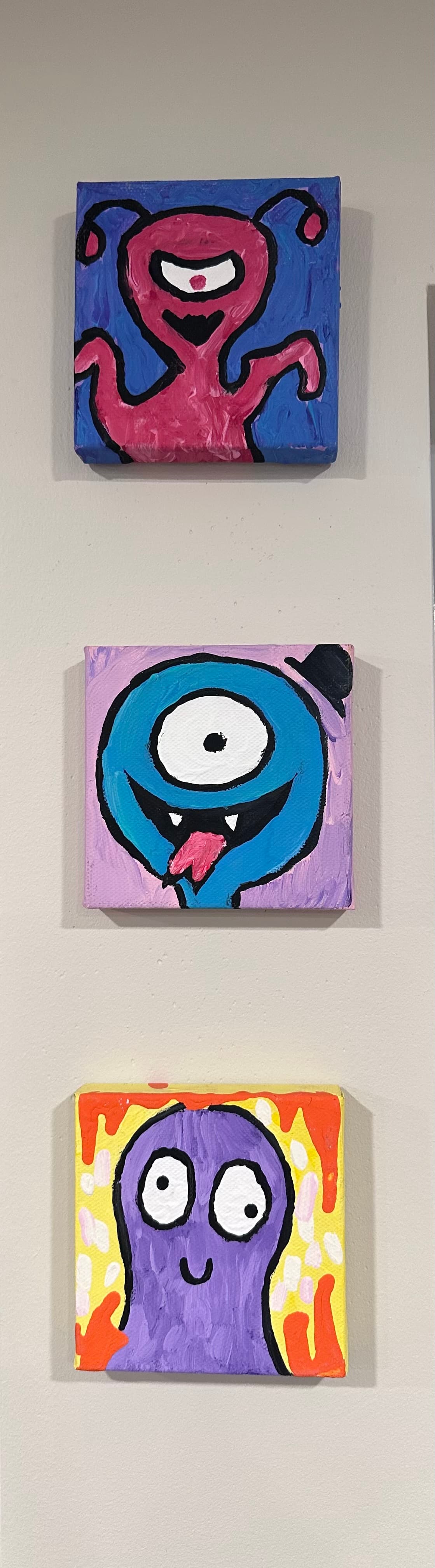 three square paintings of monster faces