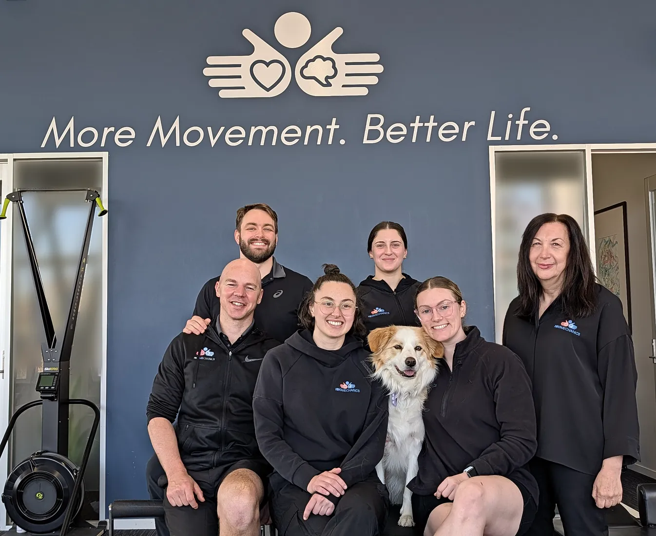 Our Footscray team with one of the clinic dogs, in front of the More Movement. Better Life. wall