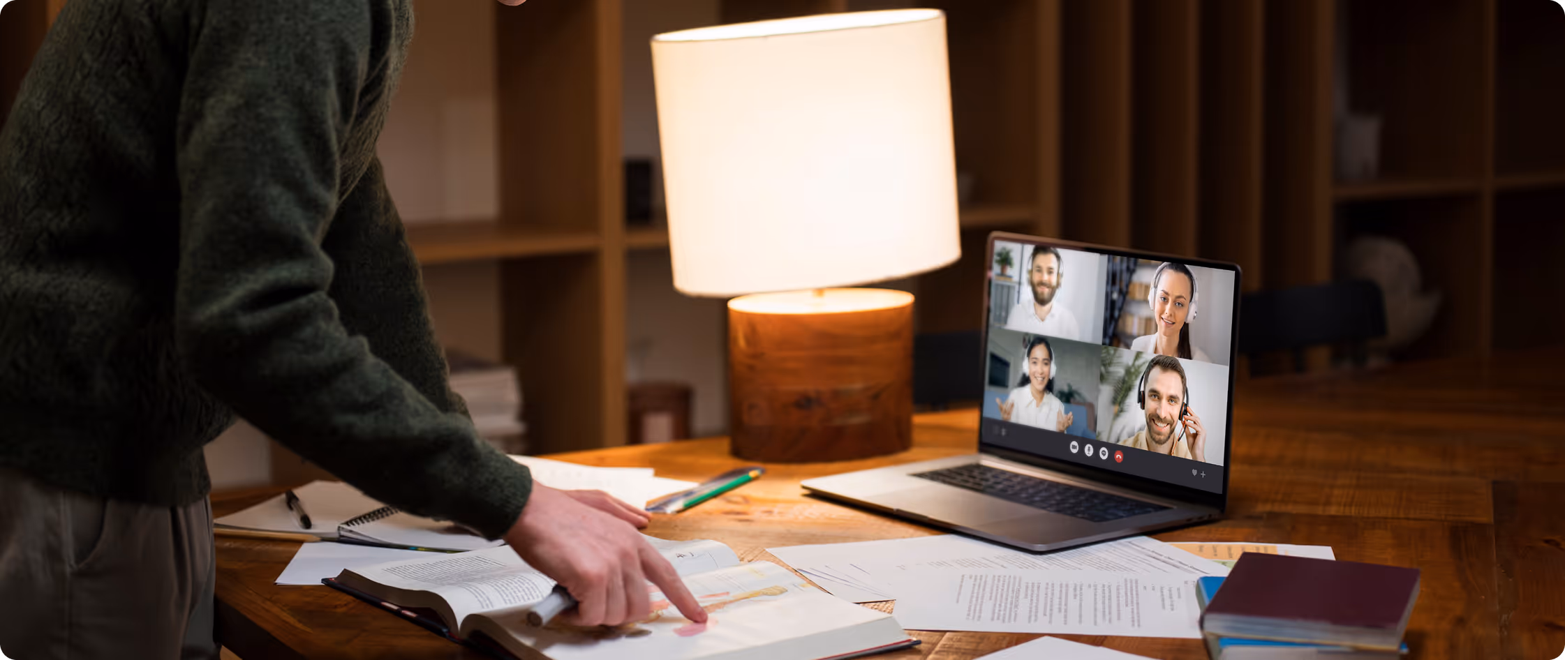 Person pointing at anatomy book while having a video call with four people on a laptop.