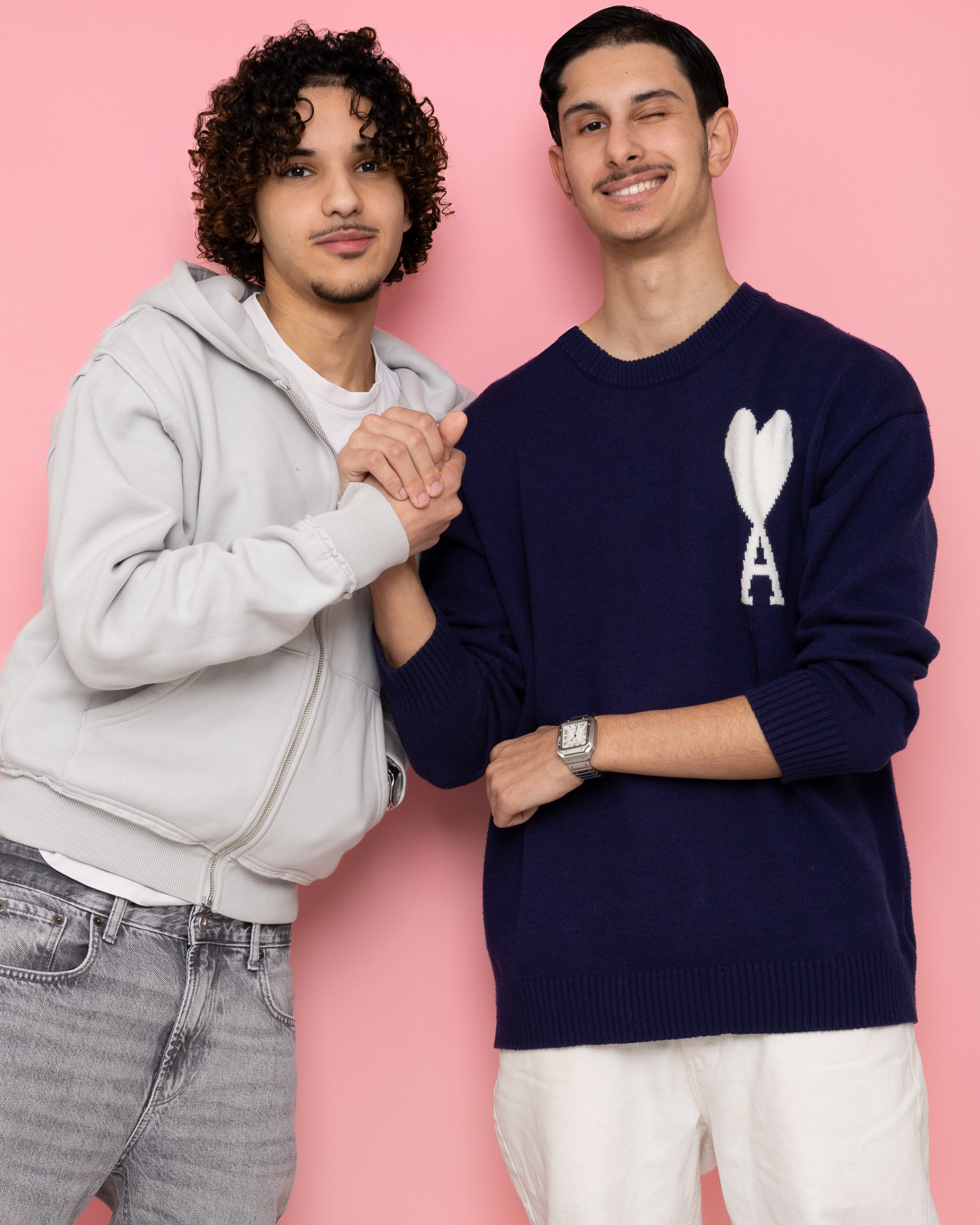 Deux jeunes hommes souriants se donnant une poignée de main devant un mur rose.