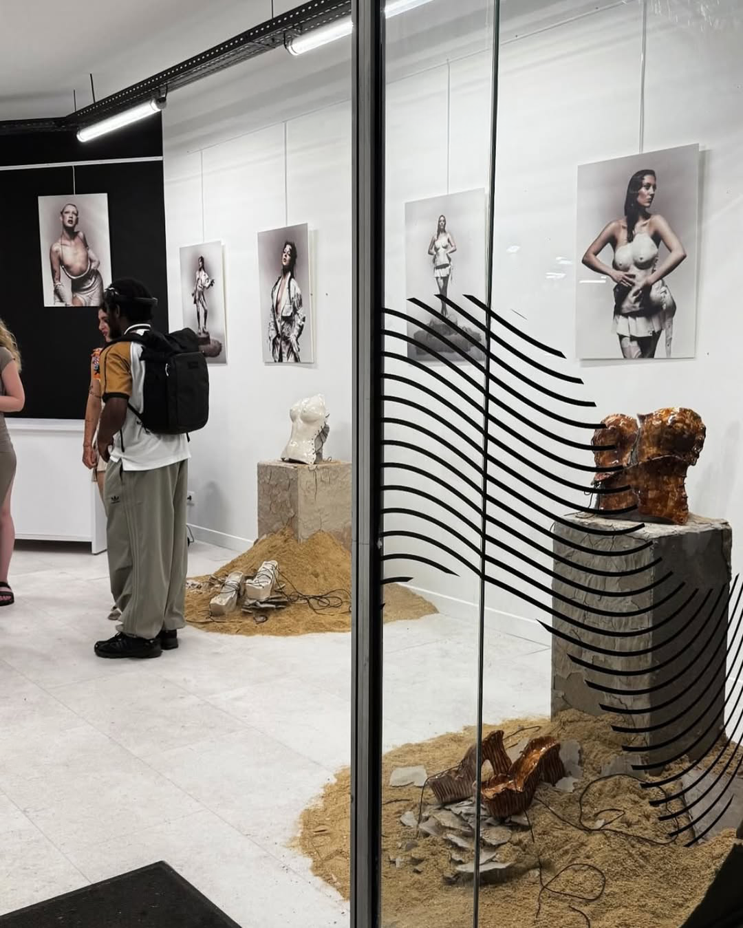 Galerie d’art avec sculptures de torses et photos de femmes nues accrochées aux murs blancs.