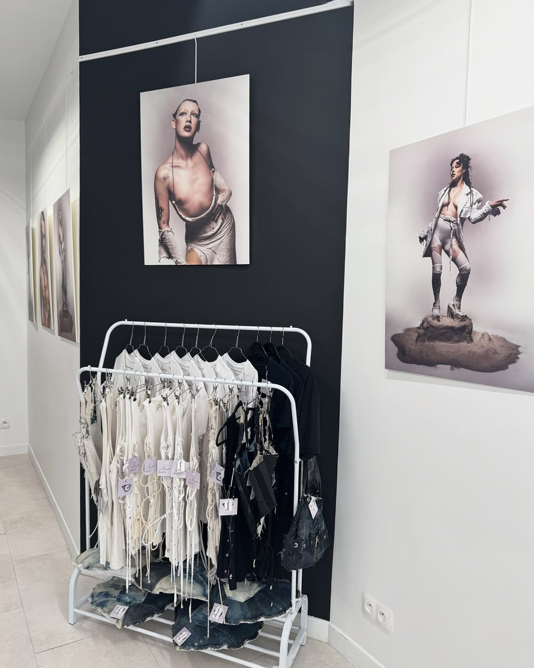 Vêtements blancs et noirs suspendus dans une pièce avec des portraits artistiques féminins aux murs.