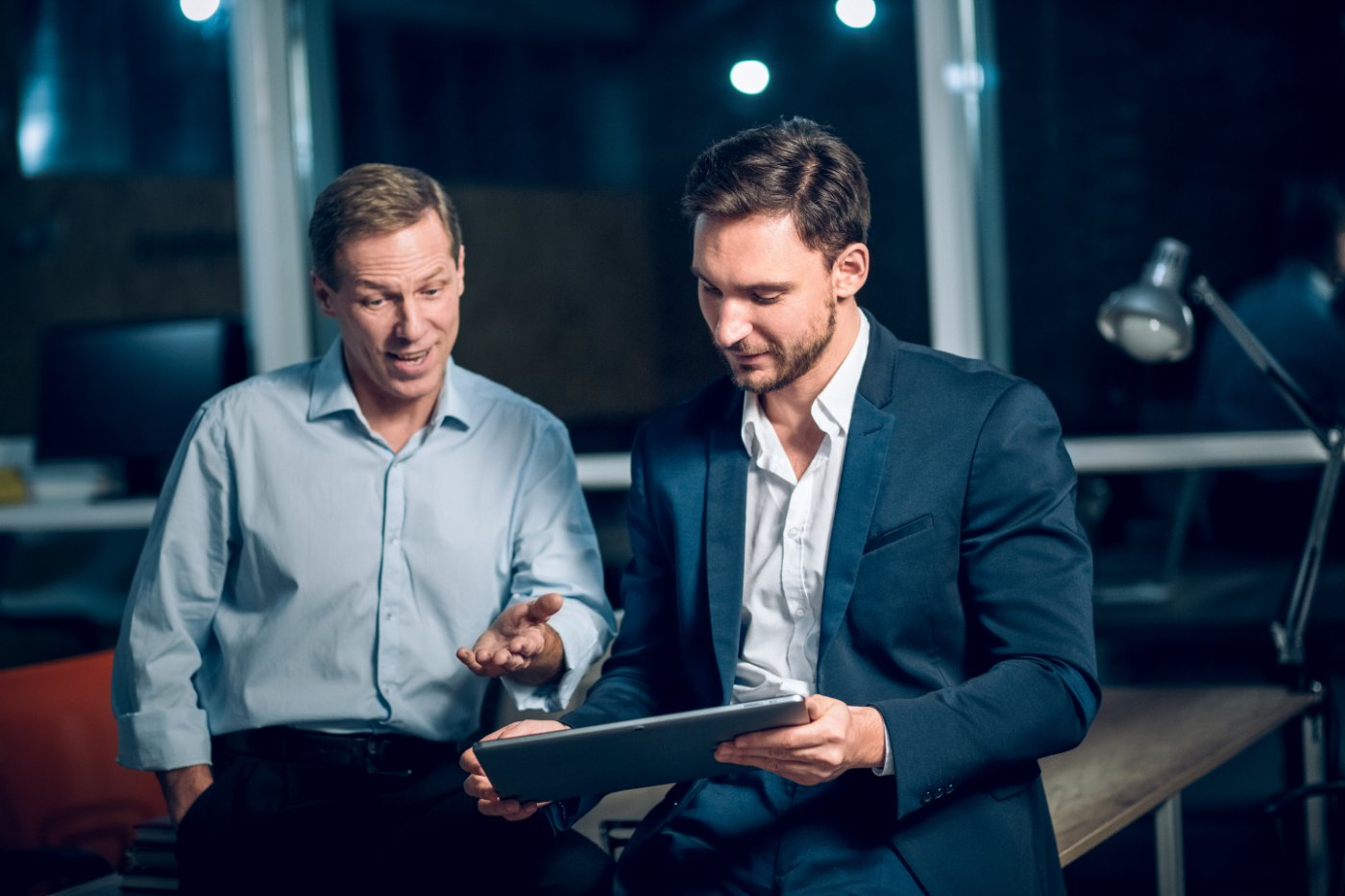 Zwei Personen besprechen abends im Büro einen Text auf einem Tablet