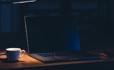 Dunkler Schreibtisch mit beleuchtetem Laptop und Kaffeetasse als Symbol für Conversion Optimierung einer Landingpage