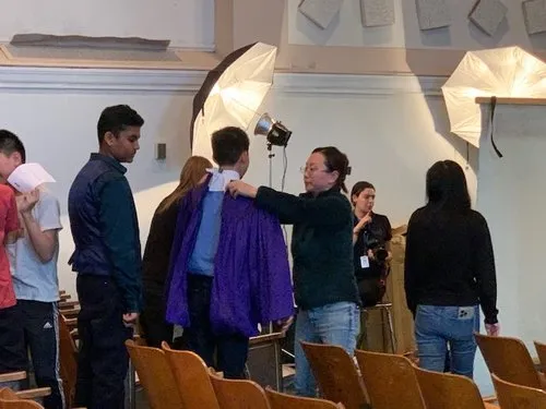 Students pose as a woman adjusts a jacket under studio lights.