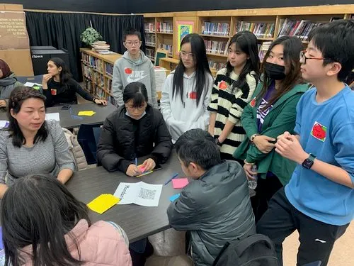 Students gather around a table in a library classroom discussing notes.