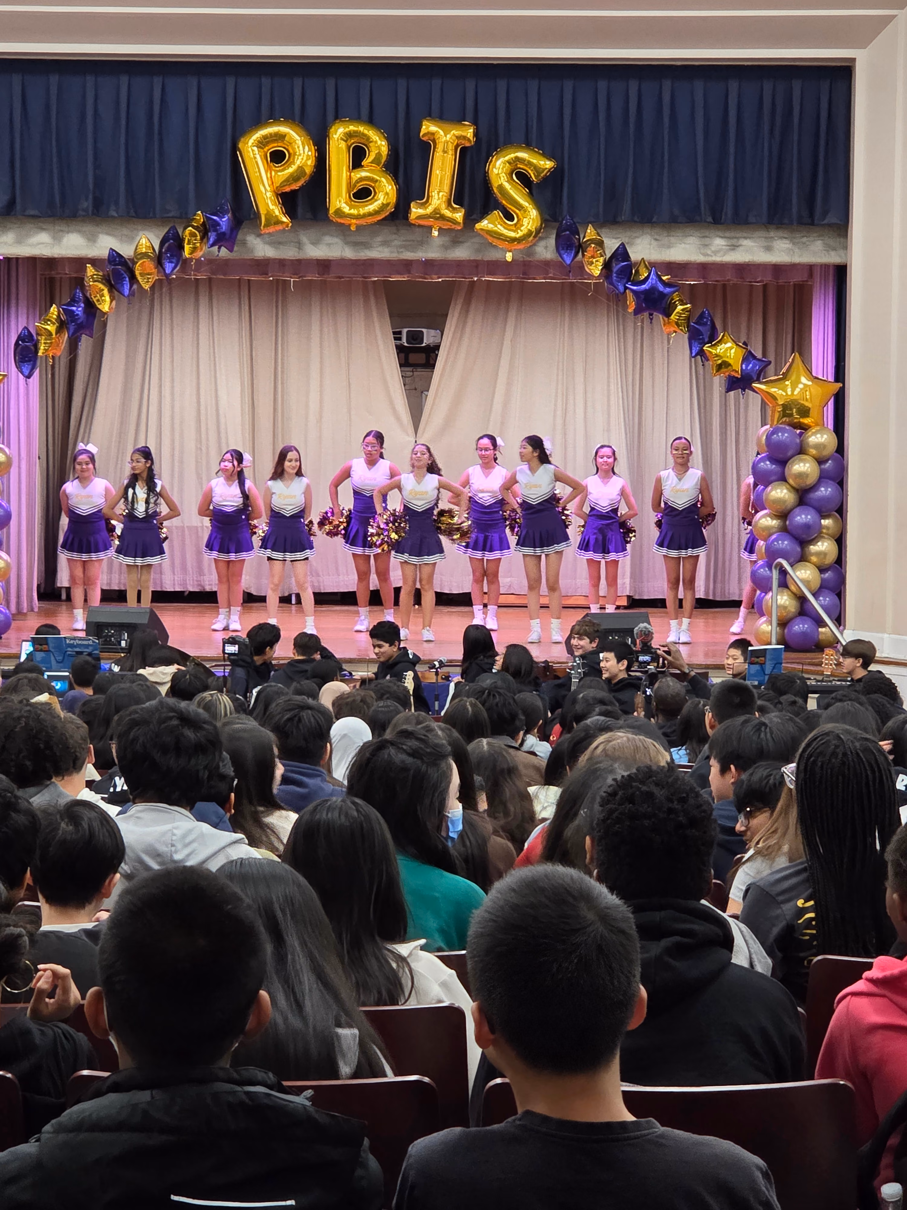 Students in purple and white perform on stage for audience