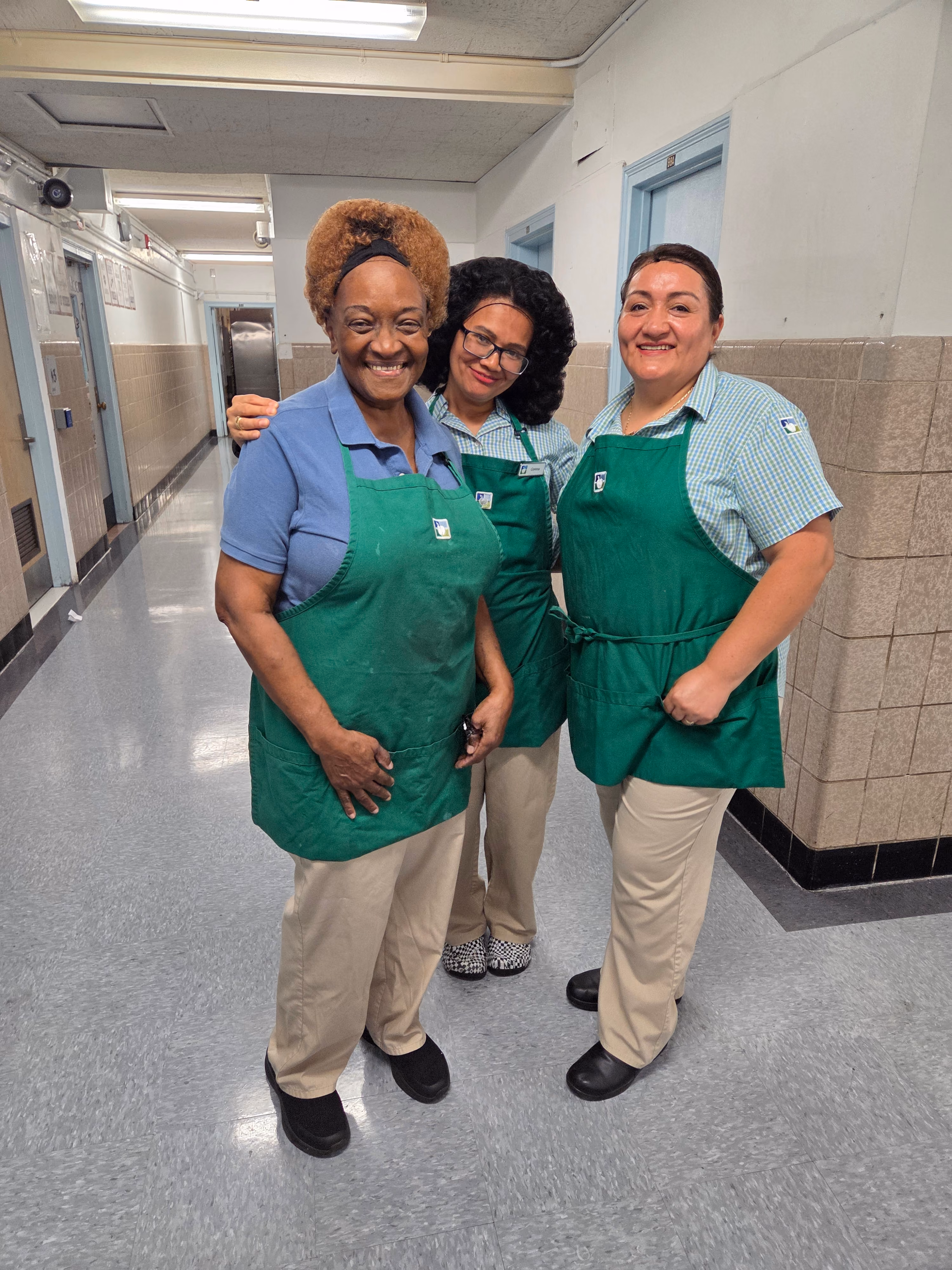Three cafeteria staff members standing together in school hallway