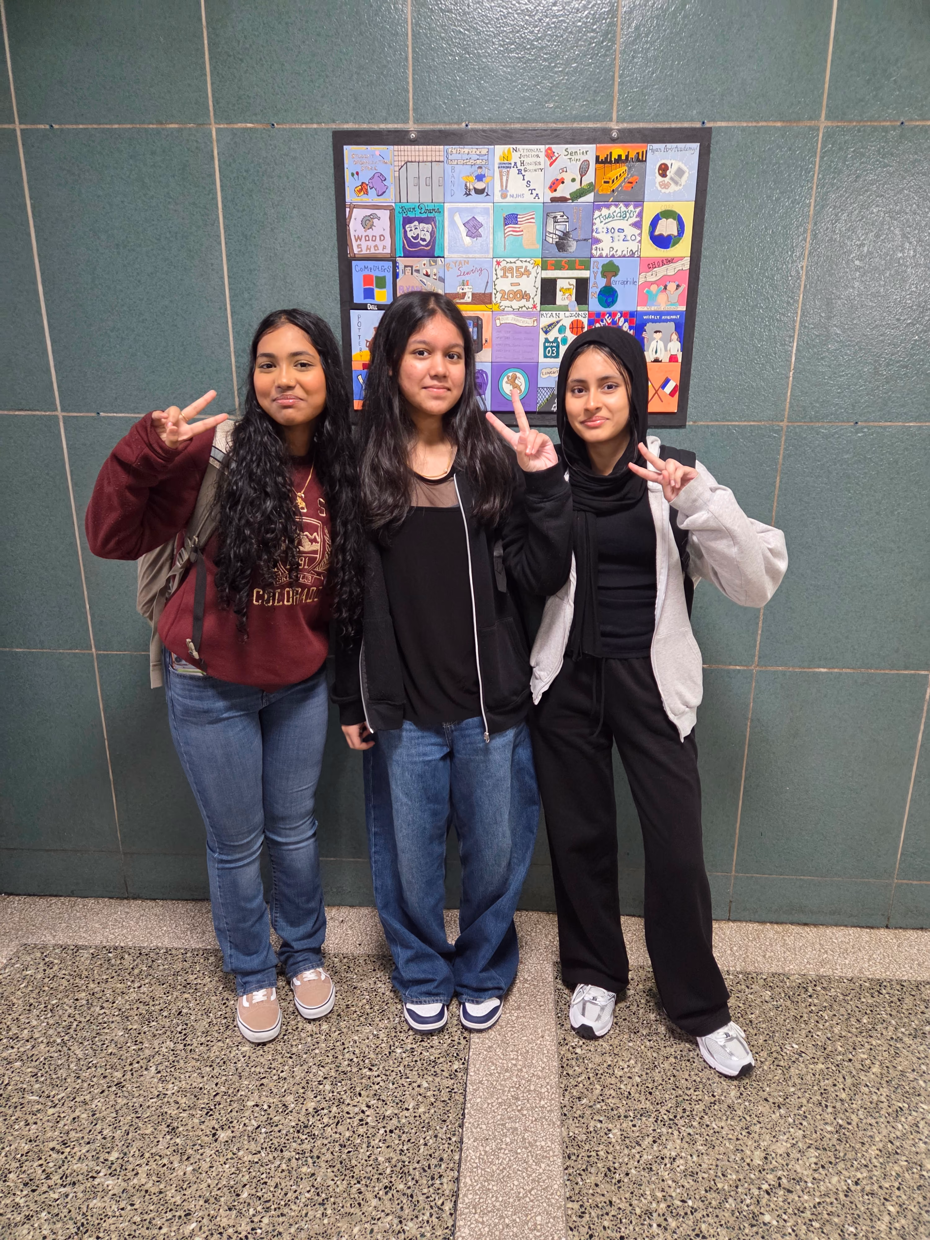 Three students posing with student artwork display board